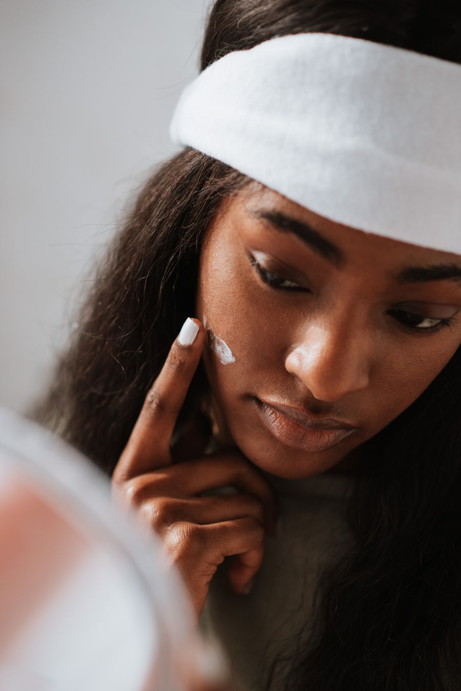 Woman in a spa headband applying face cream to her cheek