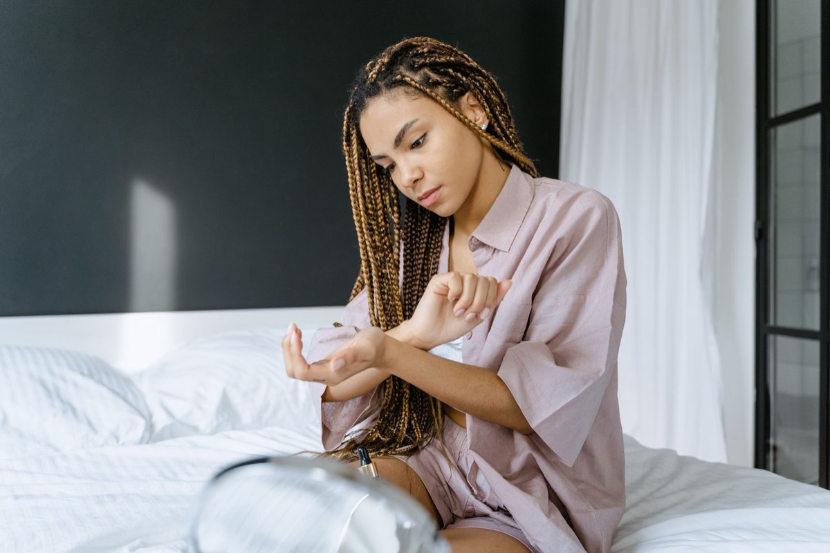 Woman with braids applying body oil to her wrist